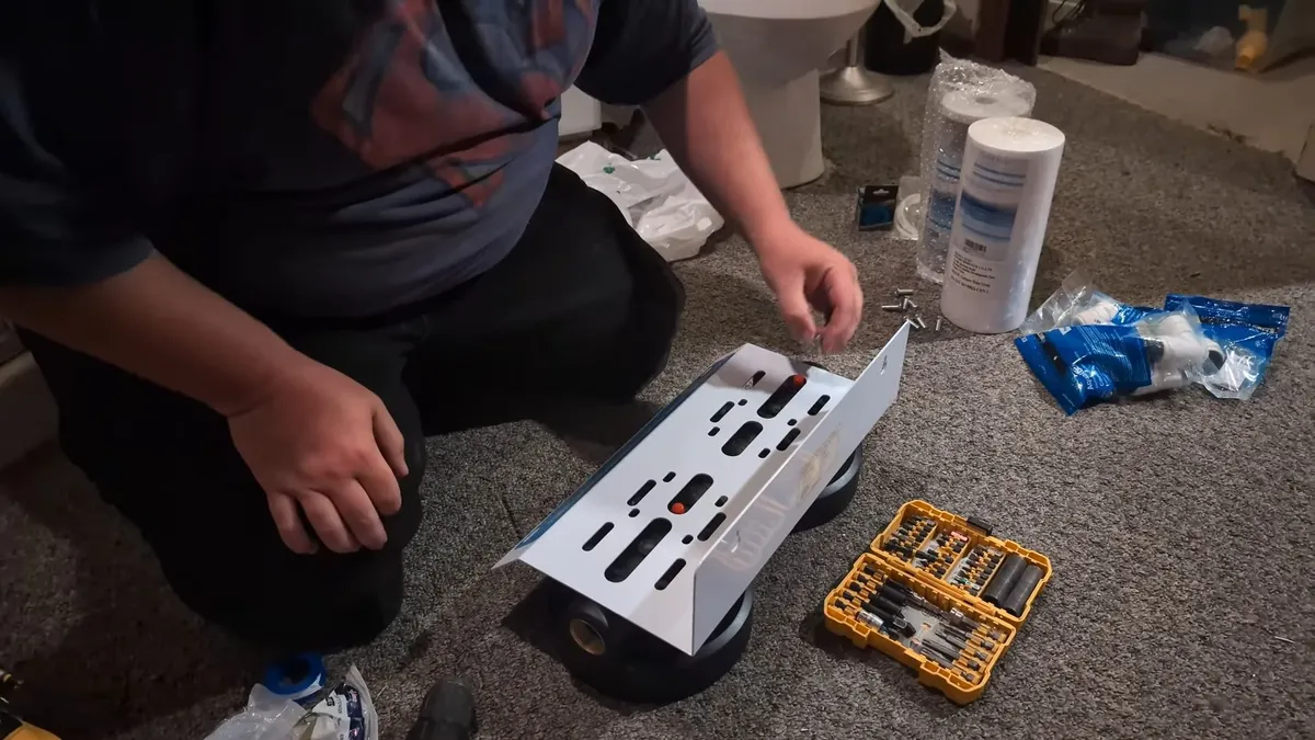 Installer assembling a two-stage whole-house filtration system on the floor during plumbing service in Asante, Surprise, AZ