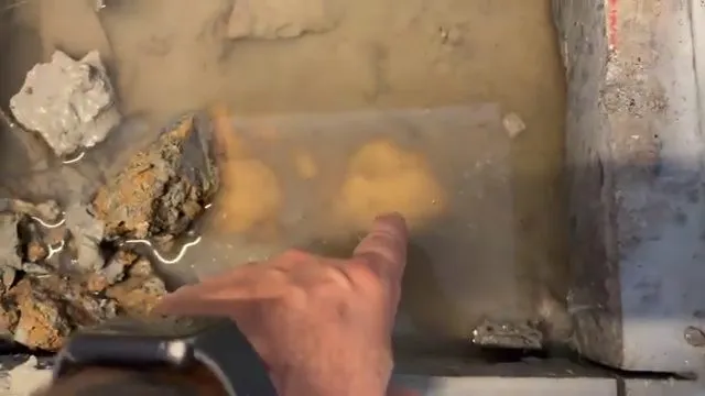 Hand pointing to water and damaged pipe exposed through a concrete slab opening during plumbing service in Mountain Vista Ranch, Surprise, AZ