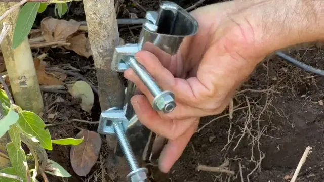 Hand holding metal pipe repair clamps beside exposed soil and roots illustrating pool leak detection: sun city grand vs marley park az
