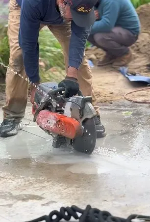 Technician cutting a concrete slab to reach buried plumbing during slab leak detection & repair