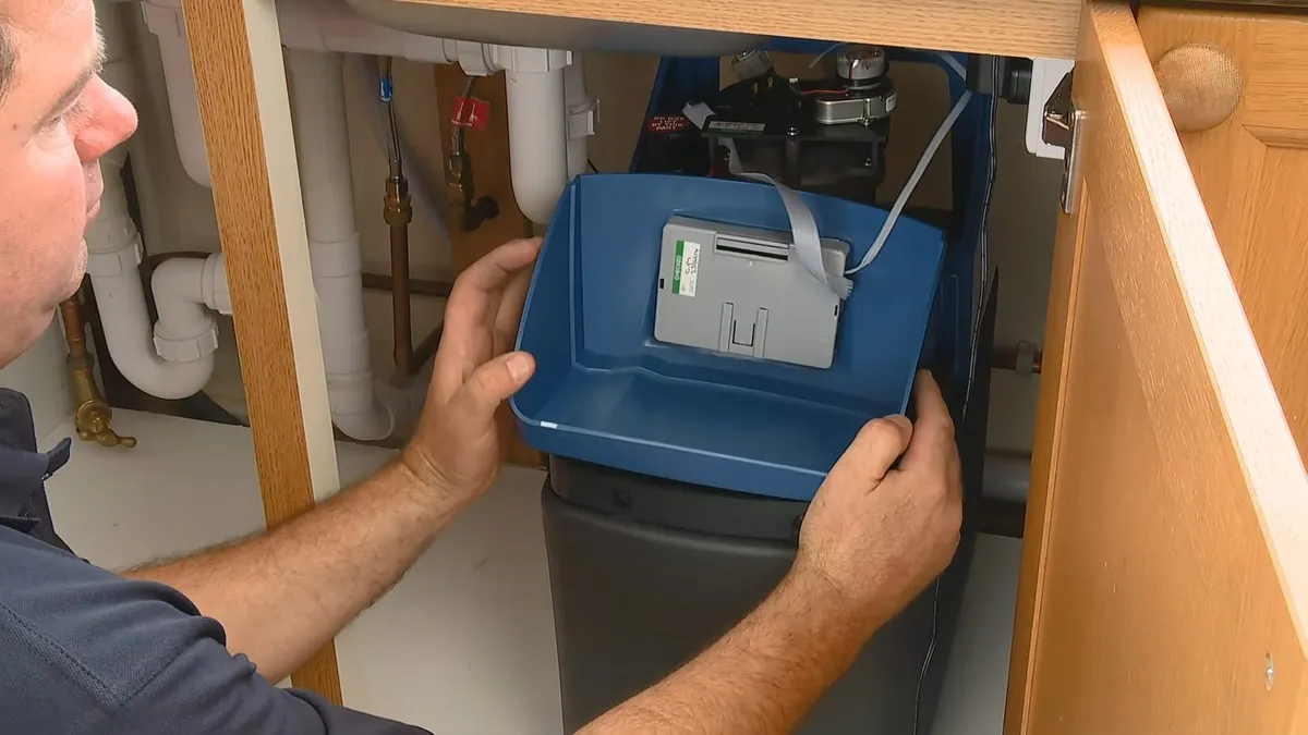 Compact blue water softener control unit positioned beneath a sink during plumbing service in Sun Village, Surprise, AZ